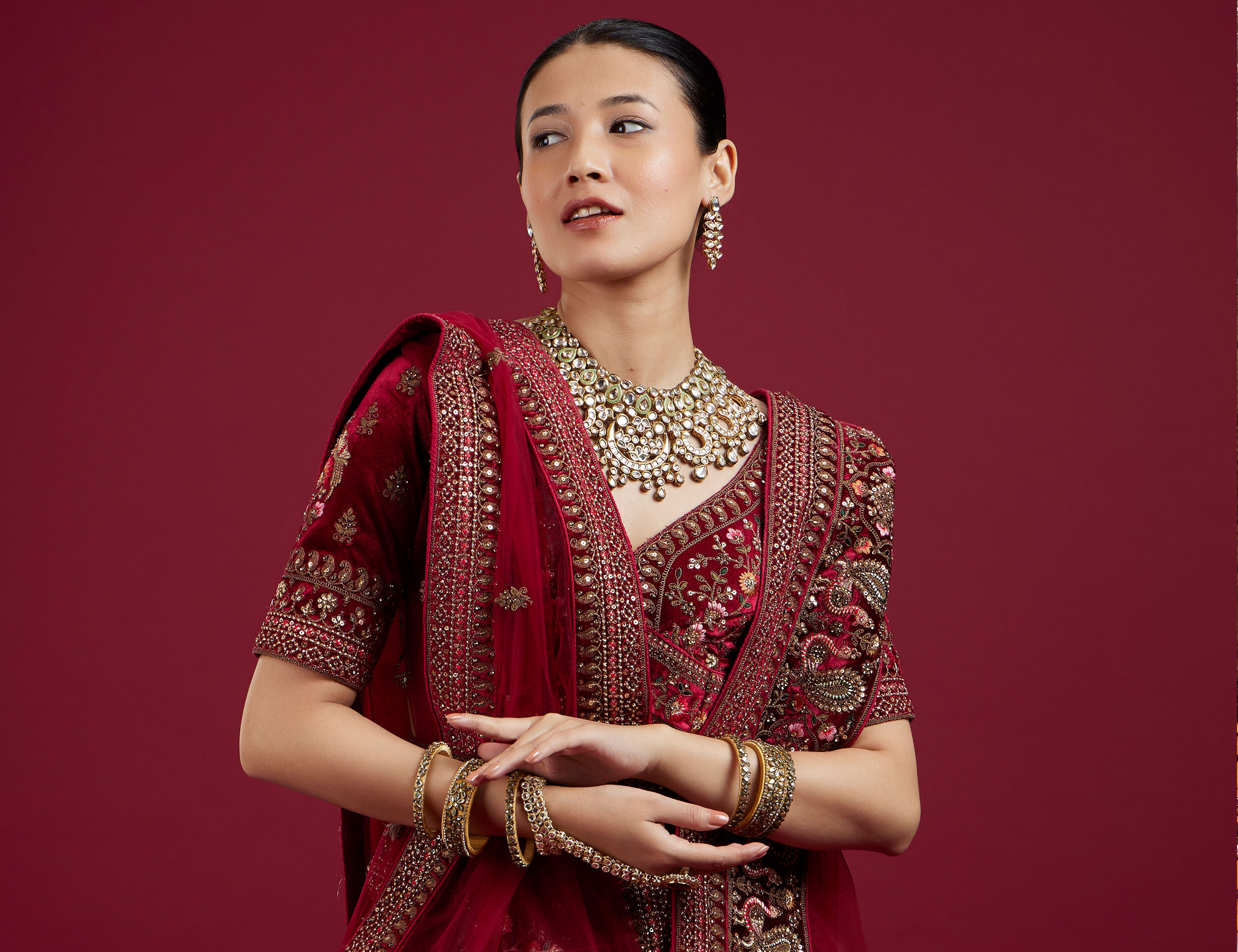 Woman in a maroon embellished saree with heavy gold jewellery and bangles styled for festive Durga Puja look